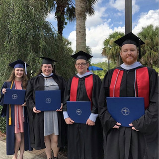 Group of four graduates holding their degrees in front of trees