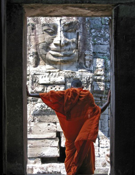 Man in Asian robes standing in doorway bowing head in front of a wall statue
