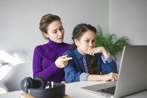 A mother and daughter are completing an assignment on a laptop.