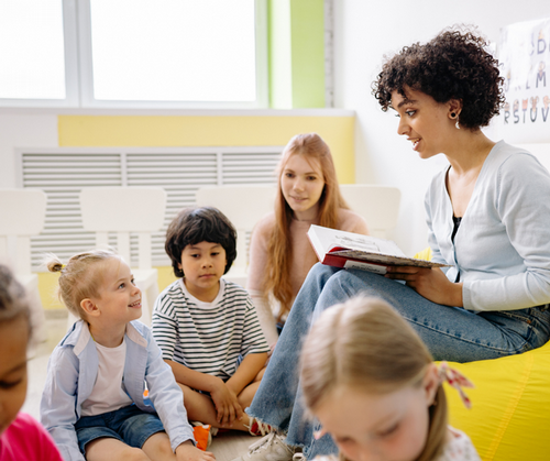 A teacher sits with a small group as she reads a book.