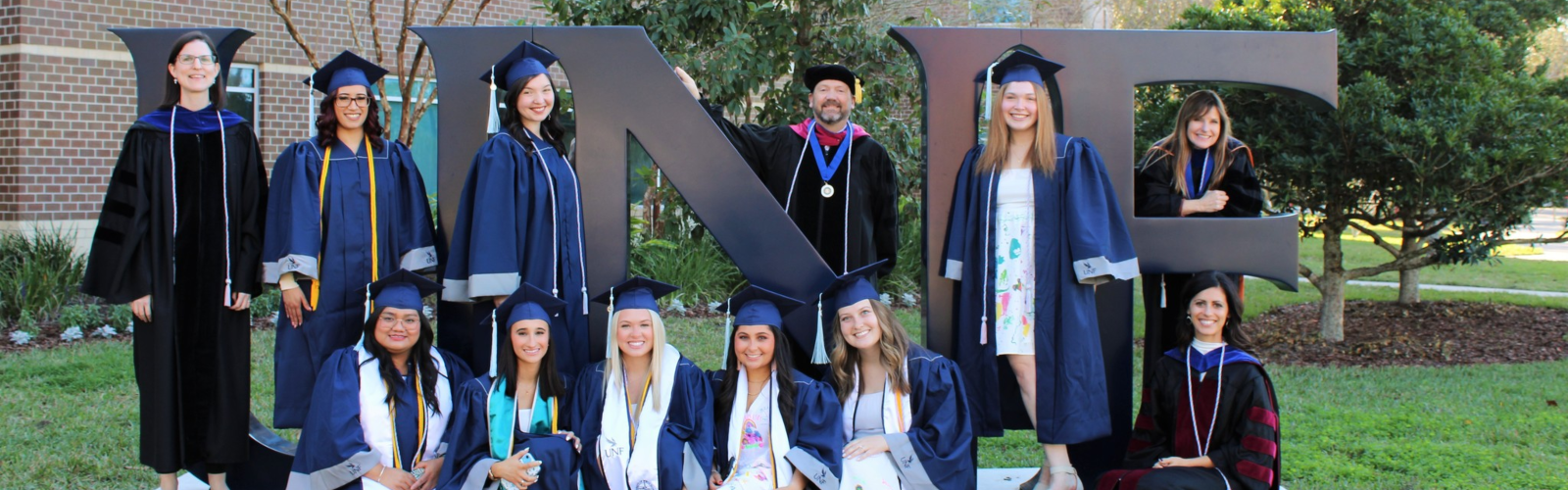 Group of COEHS graduates in front of UNF sign in their caps and gowns
