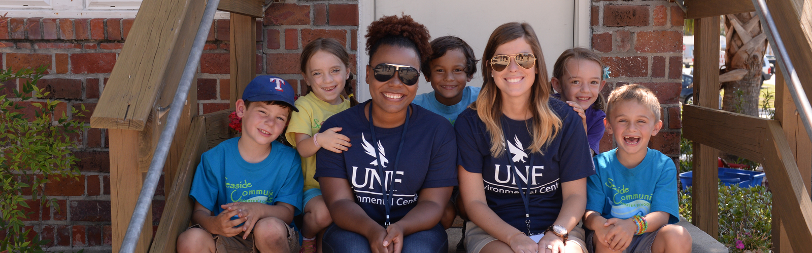 Two UNF students sitting beside a group of young kids all smiling
