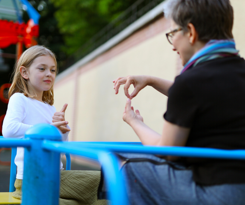A student and teacher communicate using ASL on the playground.