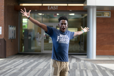 UNF male student in a UNF tshirt holding his arms out wide and looking excited