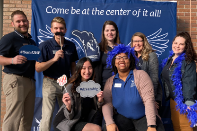 UNF staff in a photo booth holding props and smiling