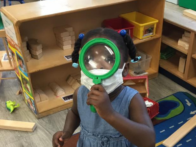 Little girl holding up a magnifying glass to her face looking at the camera