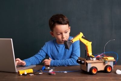 Small boy looking at a toy bulldozer and using a laptop