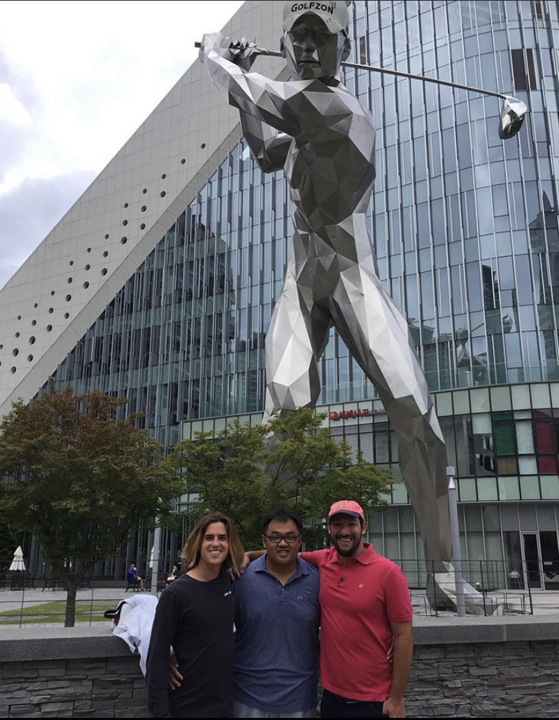 Two students with Dr. Wanyong Choi pose with a statue at Golfzon Headquarters during 2019 South Korea Study Abroad trip