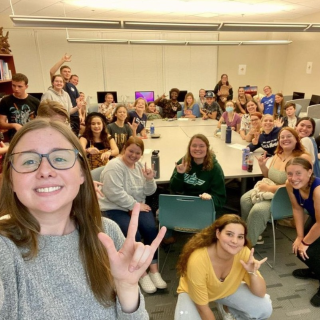 A photograph of students smiling and signing in the ASL Lab during a UNF Signing Osprey club meeting.