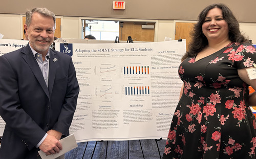 A man and woman stand in front of a poster on ELL student strategies.