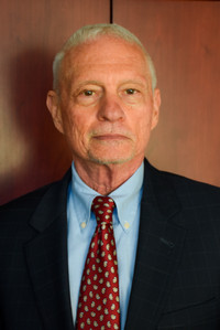 Person in suit and tie standing before a wooden paneled wall.