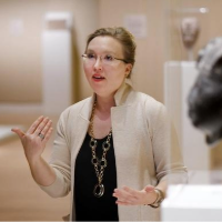 Headshot of Holly Keris, in museum giving a speech. 