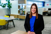 Woman in blue shirt and black blazer sitting  down and smiling 