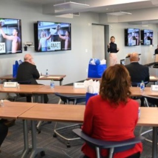 A women giving a presentation with people sitting at desks in business attiie