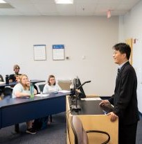 A woman giving a presentation in front of a tv with graphs to an audience