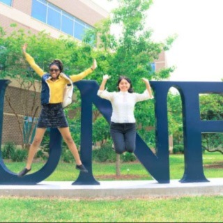 Two girls jumping in the air with the UNF sign in the background with trees and a building
