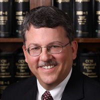 A Headshot photo of Mark Shorstein standing in front of a bookshelf.