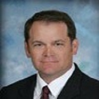 A Headshot photo of Rob Loverich in a suit with a blue background.