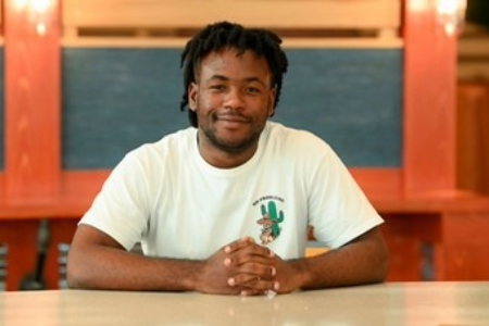 Damien sitting in a desk and smiling for the picture