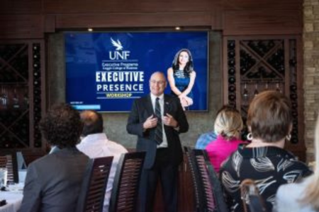 Dean Buttimer talking to a group with UNF Executive Presence on the TV