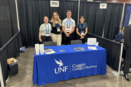 four unf students at a table with a blue table cloth and the UNF Coggin College of Business Logo