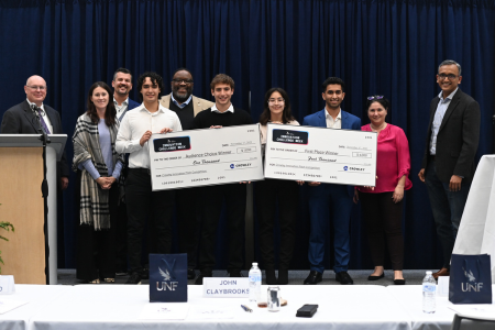 4 winners of the innovation challenge with two giant checks surrounded by 6 faculty/mentors
