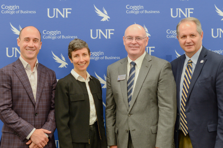 4 people in business attire smiling with a blue UNF Coggin college of Business backdrop