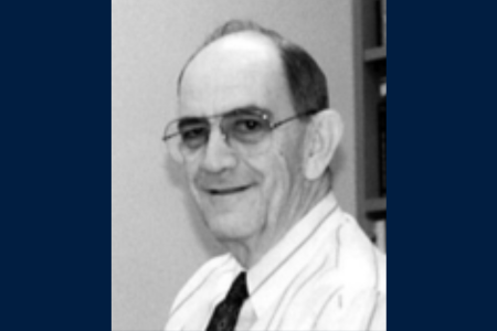 A black and white headshot of a man with a collared shirt and tie wearing glasses