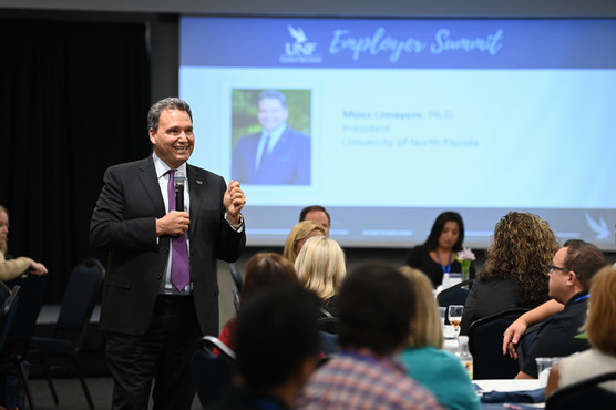 President Moez Limayem in a suit giving a presentation titled Employer Summit to an audience 