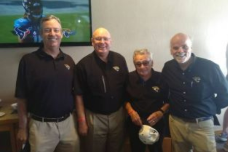 Four people smiling with a Jaguar game on TV