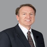 Headshot of David Walton with a suit and brown tie with a gray background