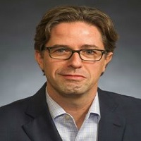 Headshot of Jason Parry with a black blazer, blue shirt and glasses with a gray background