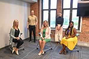 3 women sitting and a man and woman standing behind them in business attire