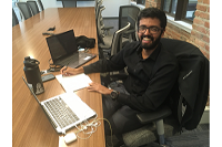 Riju Thomas working at a desk with 2 laptops, and notebook wearing black business attire