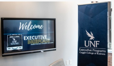 A tv with welcome executive briefcase and a sign with UNF logo and executive programs coggin college of business written on it