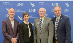 4 people in business attire smiling with a blue UNF Coggin college of Business backdrop