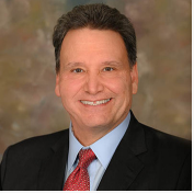 Headshot of President Moez Limayem with a red tie, blue collar shirt and black blazer with brown and white background