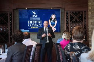 Dean Buttimer talking to a group with UNF Executive Presence on the TV