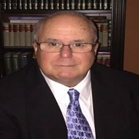 A headshot of Timothy B Bell with a suit and tie with a bookcase in the background.