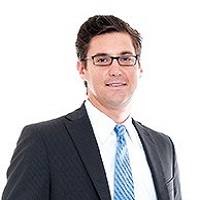 Headshot photo of Daniel Gilham wearing a suit with a blue tie and glasses