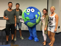 Globi the globe mascot with two guys and two girls on either side in a classroom