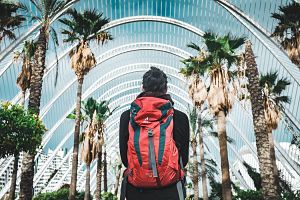 student wearing a backpack while looking at palm trees and a arch building