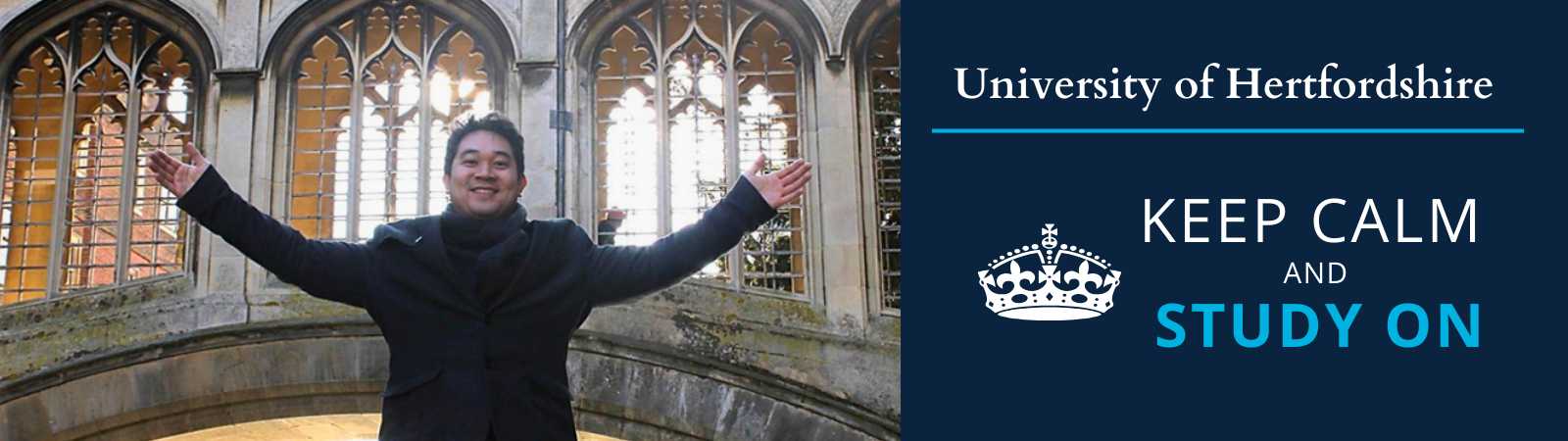 Student taking a picture in frond of the  University of Hertfordshire building, with wide open hands and a happy face. 