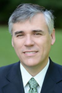 Headshot of Andres Gallo wearing suit and green tie with green blurred background