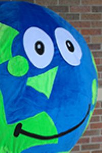 Headshot of Globi that is a mascot of a globe with eyes and smile with brick background