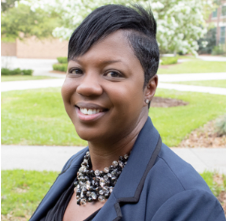 headshot of jennifer jackson wearing a beaded necklace and blazer with unf campus in background