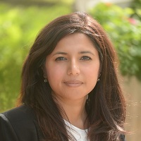 Headshot of Lakshmi Goel wearing a black blazer and a blurred green background