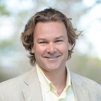 Headshot of Tobias Huning wearing a beige blazer and yellow shirt