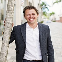 Picture of John Duda posing by a tree with a black blazer and white shirt