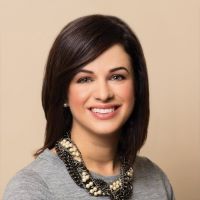 Headshot of Joanna Blinn wearing gray shirt with multicolored necklace with light brown background